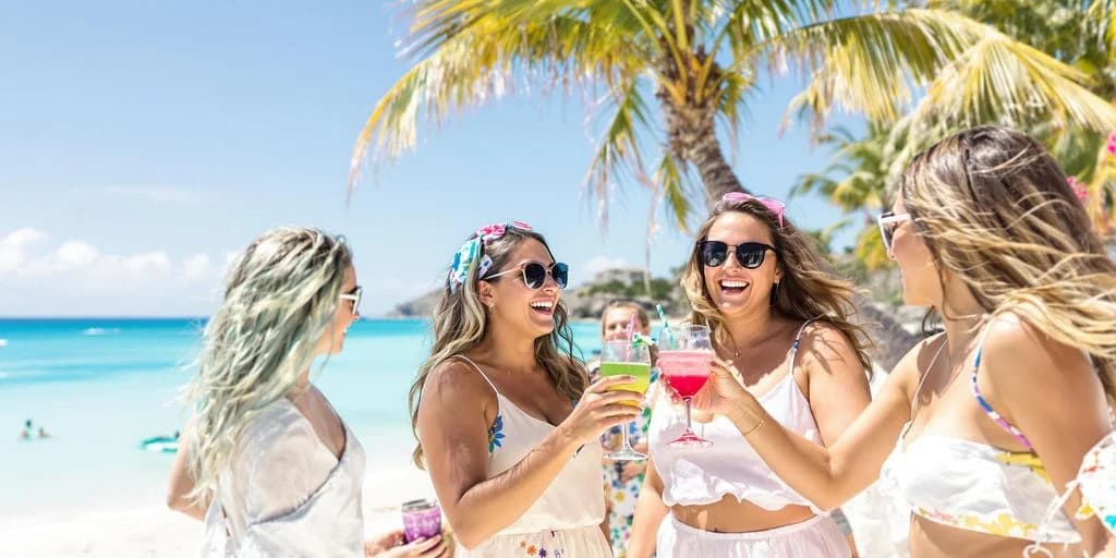 Women with cocktails at Cabo Bachelorette First-Timers: What You Need to Know on beach with palm trees
