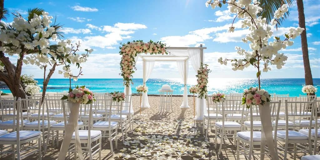 Beach wedding ceremony at Cabo Wedding Planners Who Handle 50+ Weddings Per Year with floral arch and white chairs