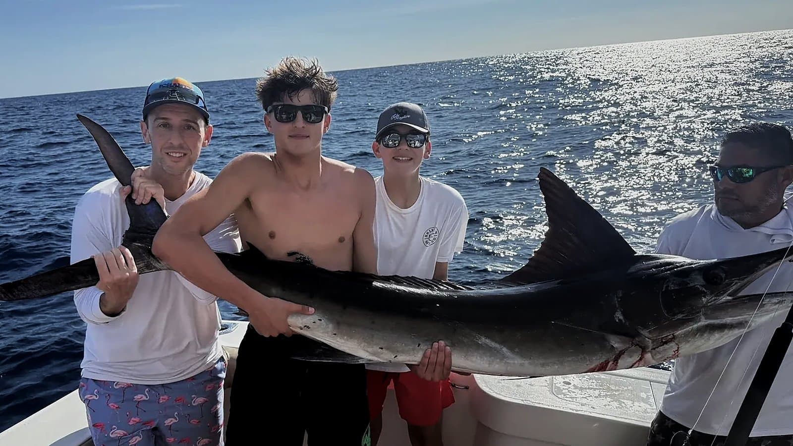 Four anglers holding a striped marlin on a sportfishing charter off Cabo San Lucas