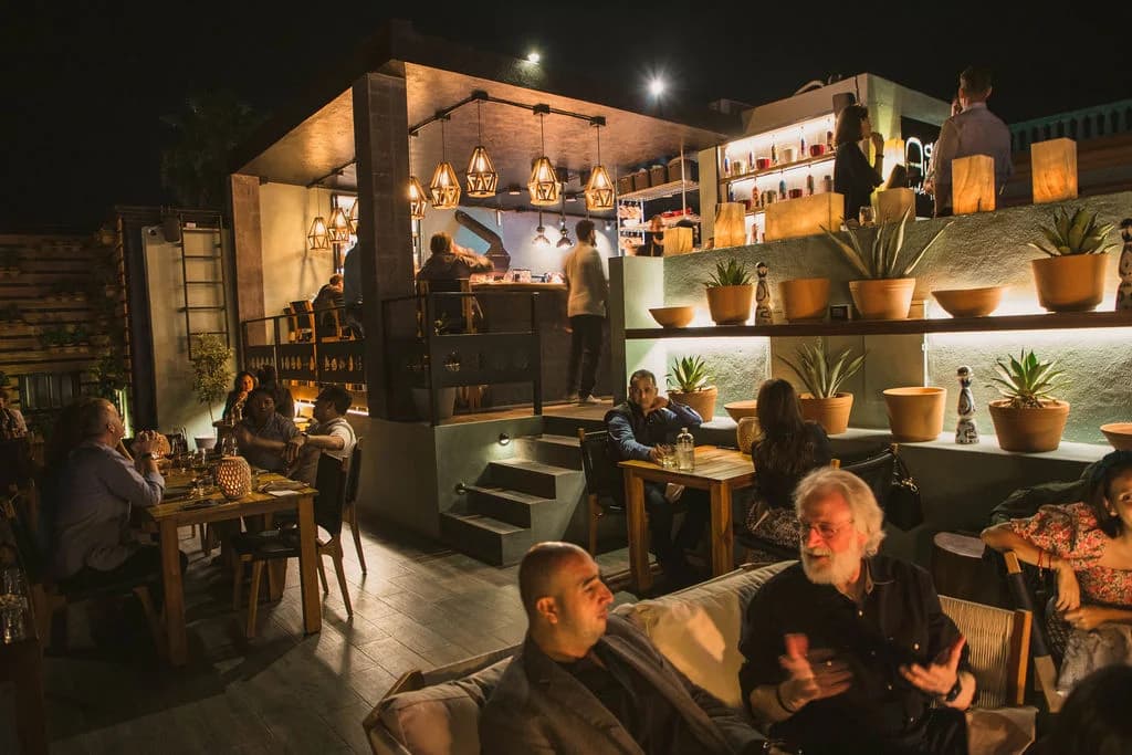 Indoor bar at AGAVE Kitchen at night, with patrons in San José del Cabo