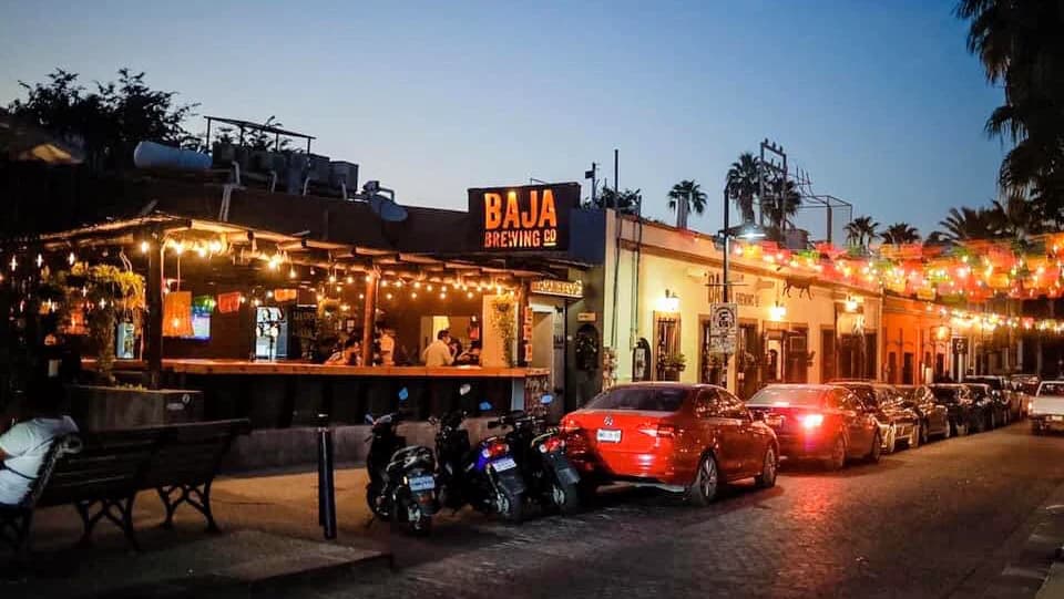 Restaurant exterior at Baja Brewing Company at dusk, with parked vehicles in San José del Cabo