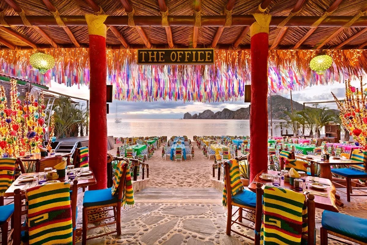 Beach restaurant at The Office with colorful tables, at dusk in Cabo San Lucas