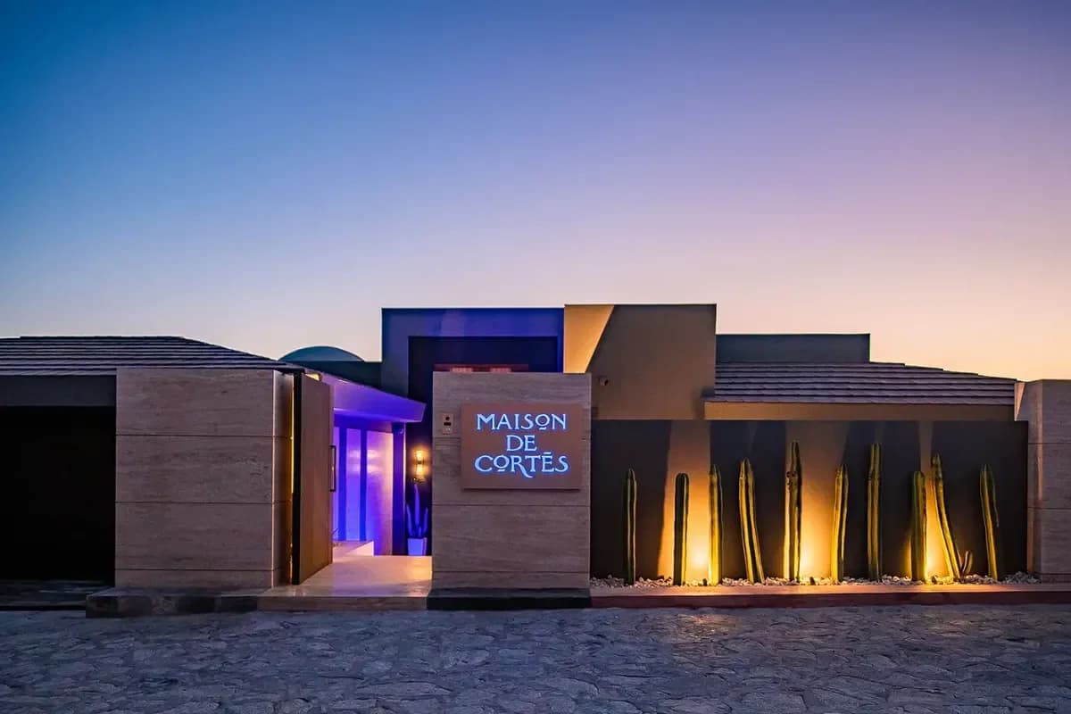 Exterior facade at Maison De Cortes at dusk, with lit sign